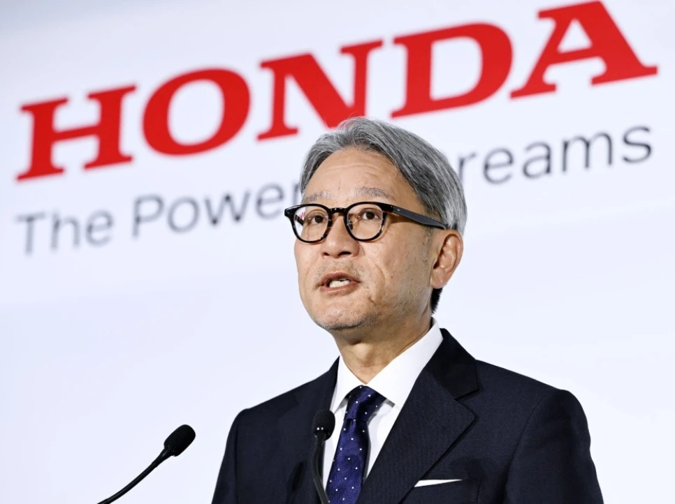 Honda CEO Toshihiro Mibe speaking at a press conference with the Honda logo and slogan "The Power of Dreams" visible in the background