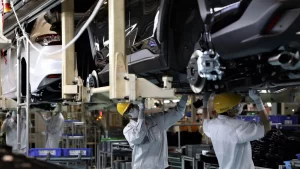 Thailand's Auto Industry Faces Continued Challenges as Production Declines for 20th Month 1 Factory workers in protective gear and yellow helmets working on vehicle assembly in a Thai automotive manufacturing plant.