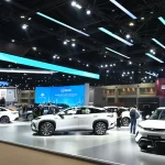 BYD electric vehicle display at an auto show featuring multiple white EVs on a sleek exhibition floor with modern blue lighting and digital screens