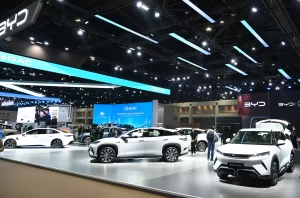 Thailand's EV Industry Calls for Flexibility Amid Missed Production Targets 1 BYD electric vehicle display at an auto show featuring multiple white EVs on a sleek exhibition floor with modern blue lighting and digital screens
