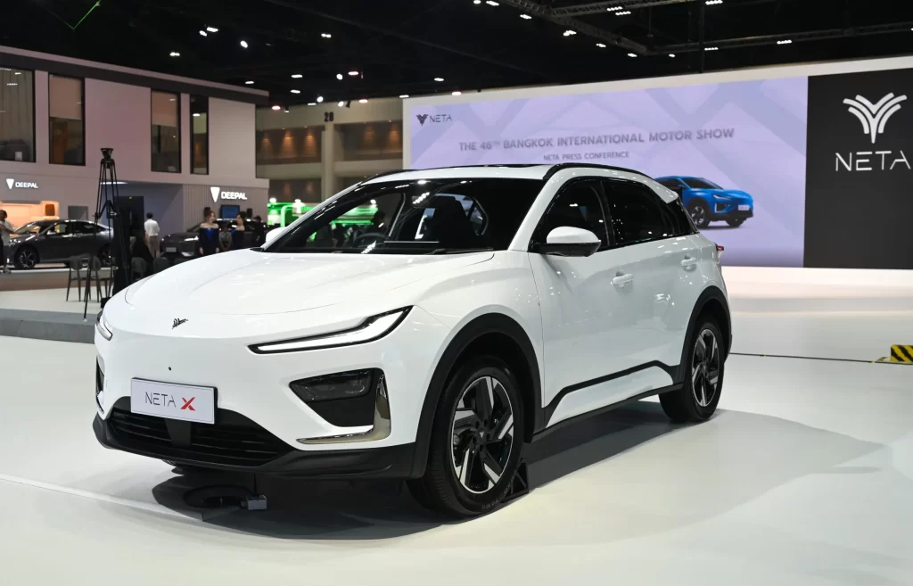 Neta X electric SUV displayed at Bangkok International Motor Show, featuring a sleek white exterior design with the Neta logo visible in the background booth