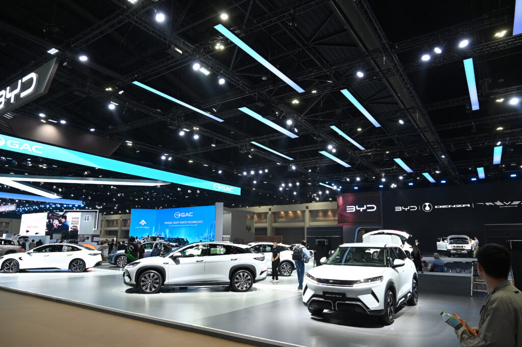 Thailand Adjusts EV Promotions to Address Market Glut 1 Electric vehicles from BYD and GAC displayed at a modern automotive exhibition hall, with visitors viewing the cars under bright overhead lighting