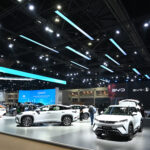 Electric vehicles from BYD and GAC displayed at a modern automotive exhibition hall, with visitors viewing the cars under bright overhead lighting